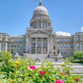Imposing stone capitol building with a dome, surrounded by greenery and vibrant pink flowers under a clear blue sky near LOCAL Boise apartments.