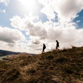 Two people walking up a grassy hill with a cloudy sky and distant landscape in the background near LOCAL Boise apartments.
