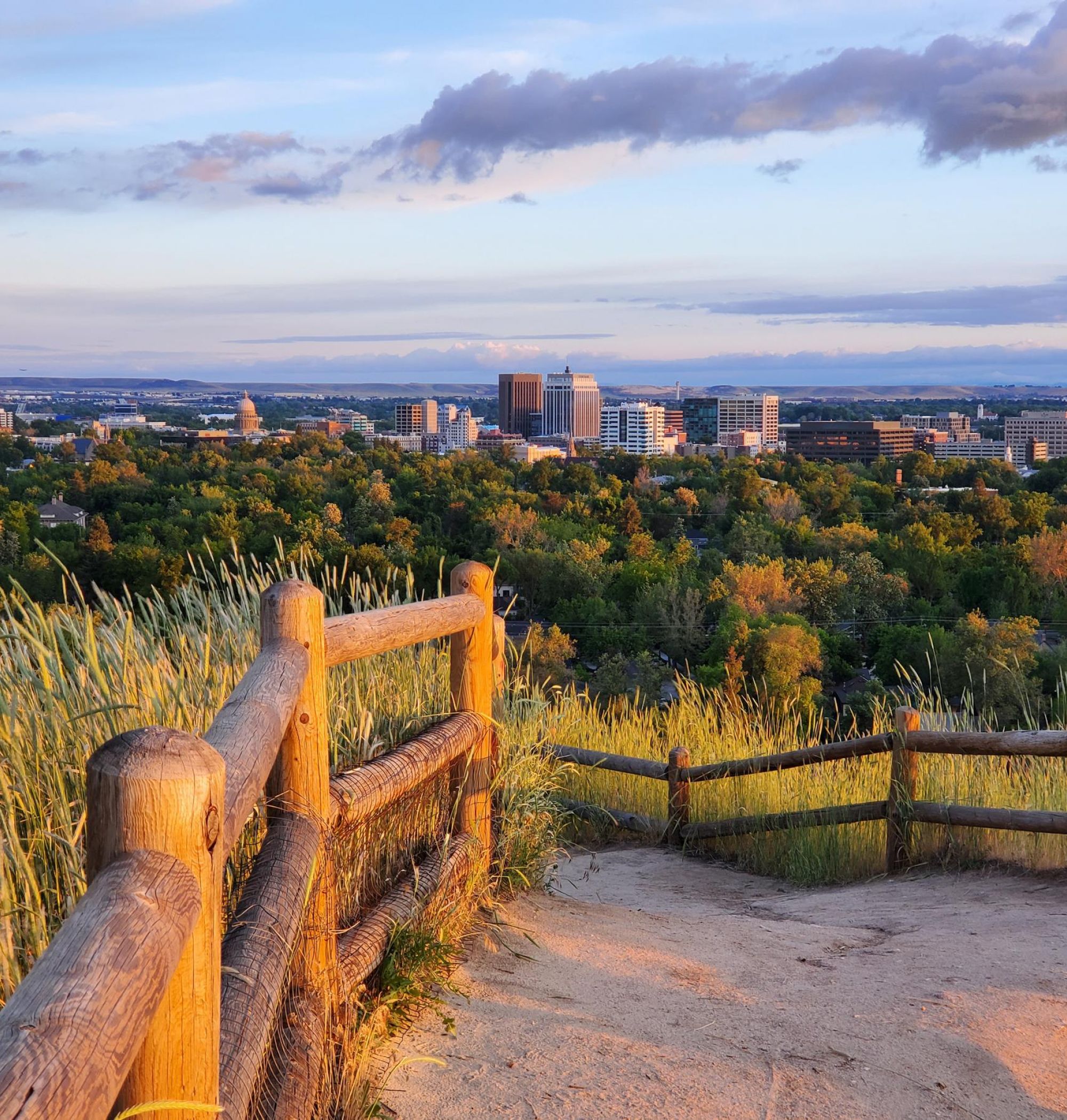 View of a city skyline at sunset from a hilltop with a wooden fence and grassy foreground near LOCAL Boise apartments.